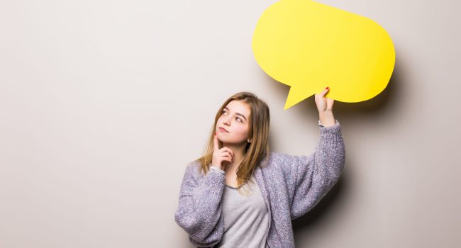 Young beautiful girl holding a yellow bubble for text, isolated on a white background