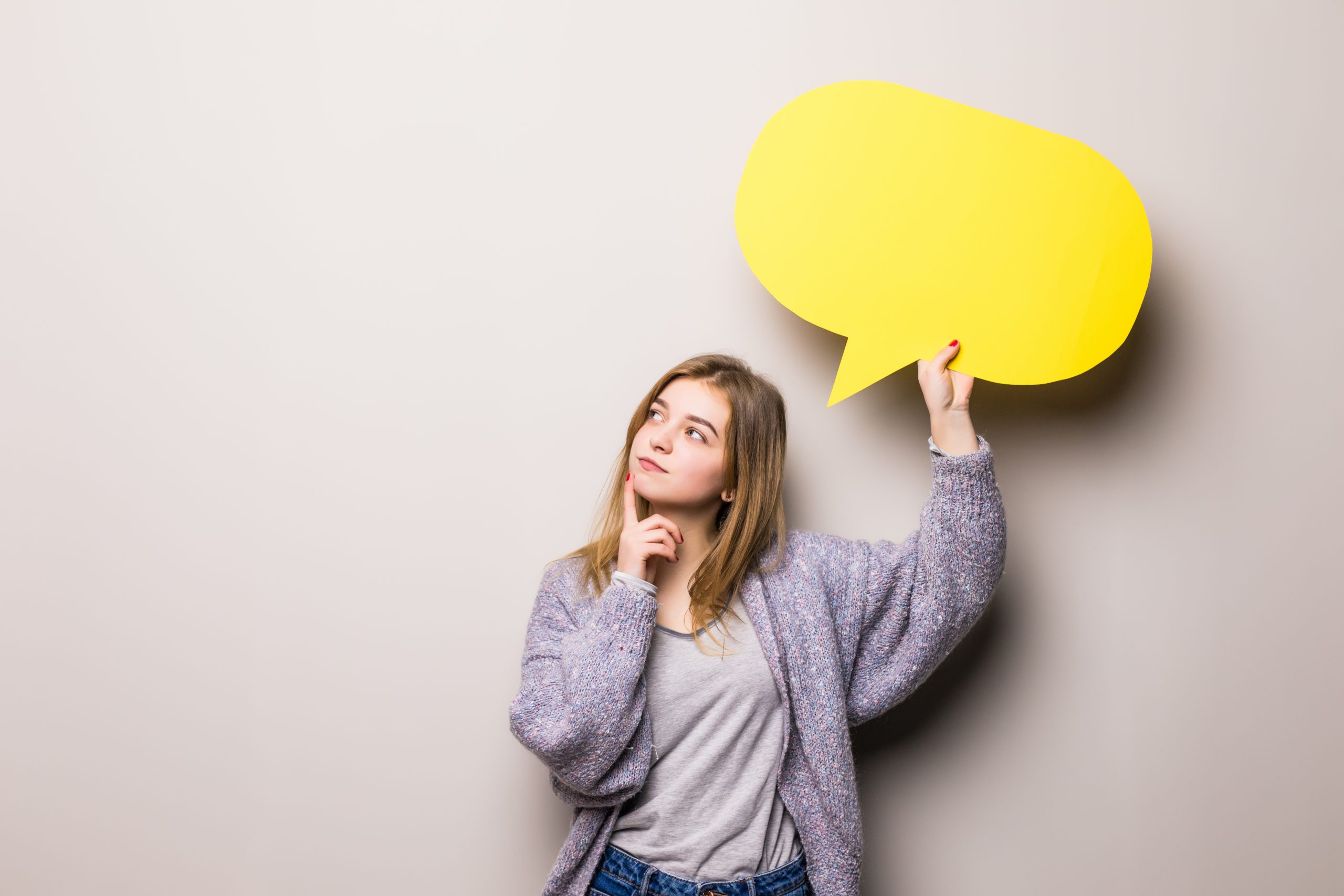 Young beautiful dreaming girl holding a yellow bubble for text, isolated on a gray background